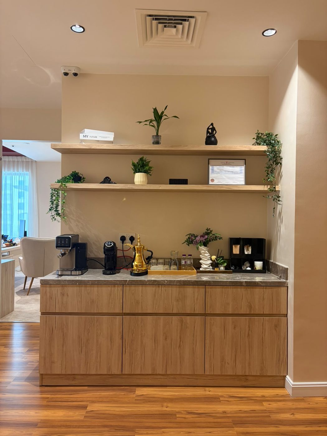 Office coffee station with handleless light-oak base cabinets, a grey stone worktop and two floating oak shelves