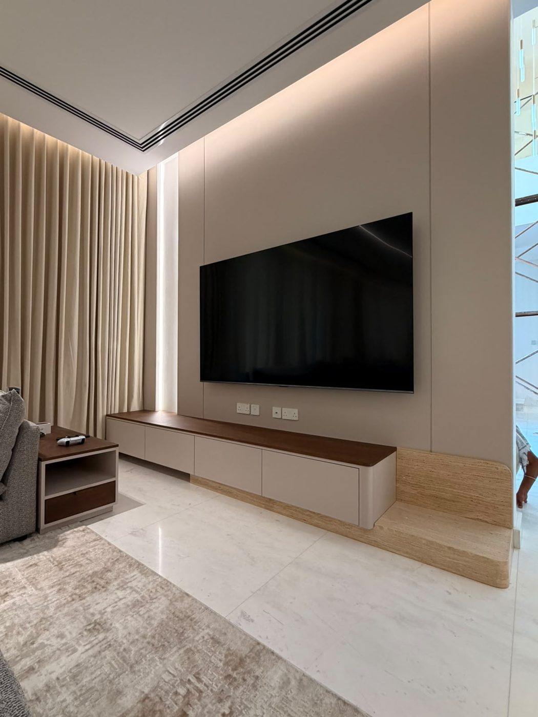 Floating TV unit with walnut top and cream cabinets beneath a wall-mounted TV and cove lighting